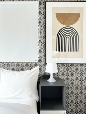 A neatly made bed with white linens, a black nightstand with a white lamp, and a framed abstract artwork on the wall. - Modern Property 15 Mins To Kumamoto Airport By Restavio (Ozu)