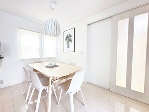 Ein zeitgemäßer Essbereich mit einem runden Tisch, weißen Stühlen, einer Pendelleuchte und einem gerahmten Kunstwerk an der Wand.