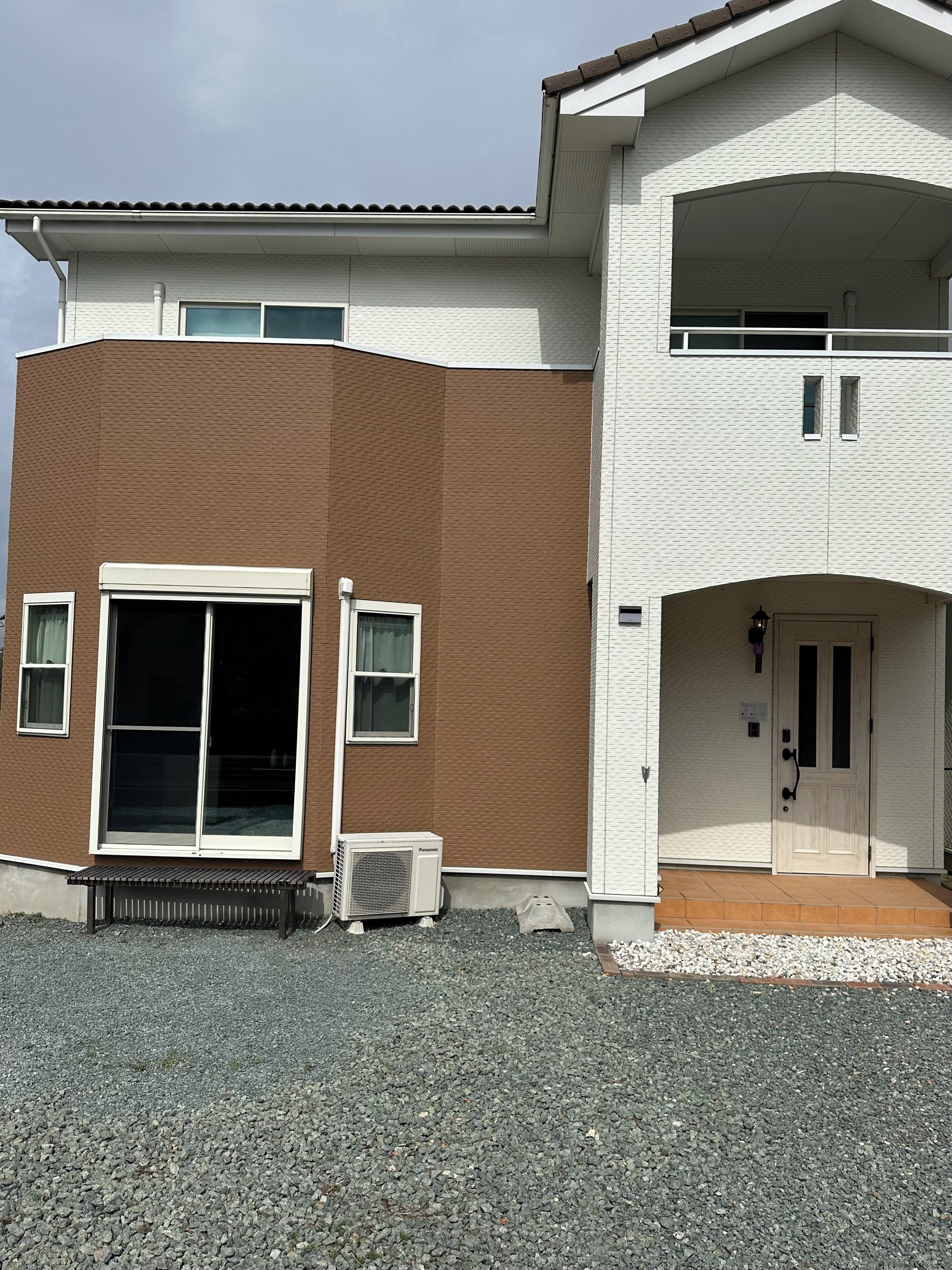 A two-story building with a brown and white exterior, a front door, and a bench outside.