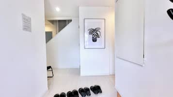 A staircase with a framed plant artwork, a white door, and a row of black shoes on the landing.