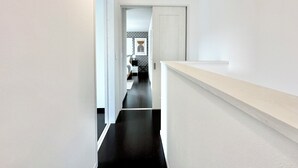 A narrow hallway with a black floor leading to a bedroom with a bed, bedside table, and a wall-mounted artwork. - Modern Property 15 Mins To Kumamoto Airport By Restavio (Ozu)