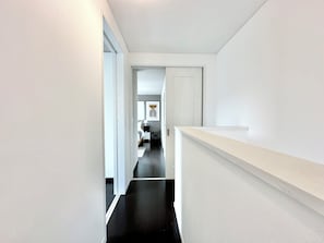 En smal hall med ett svart golv leder till ett sovrum med en säng, ett sängbord och ett konstverk som hänger på väggen.