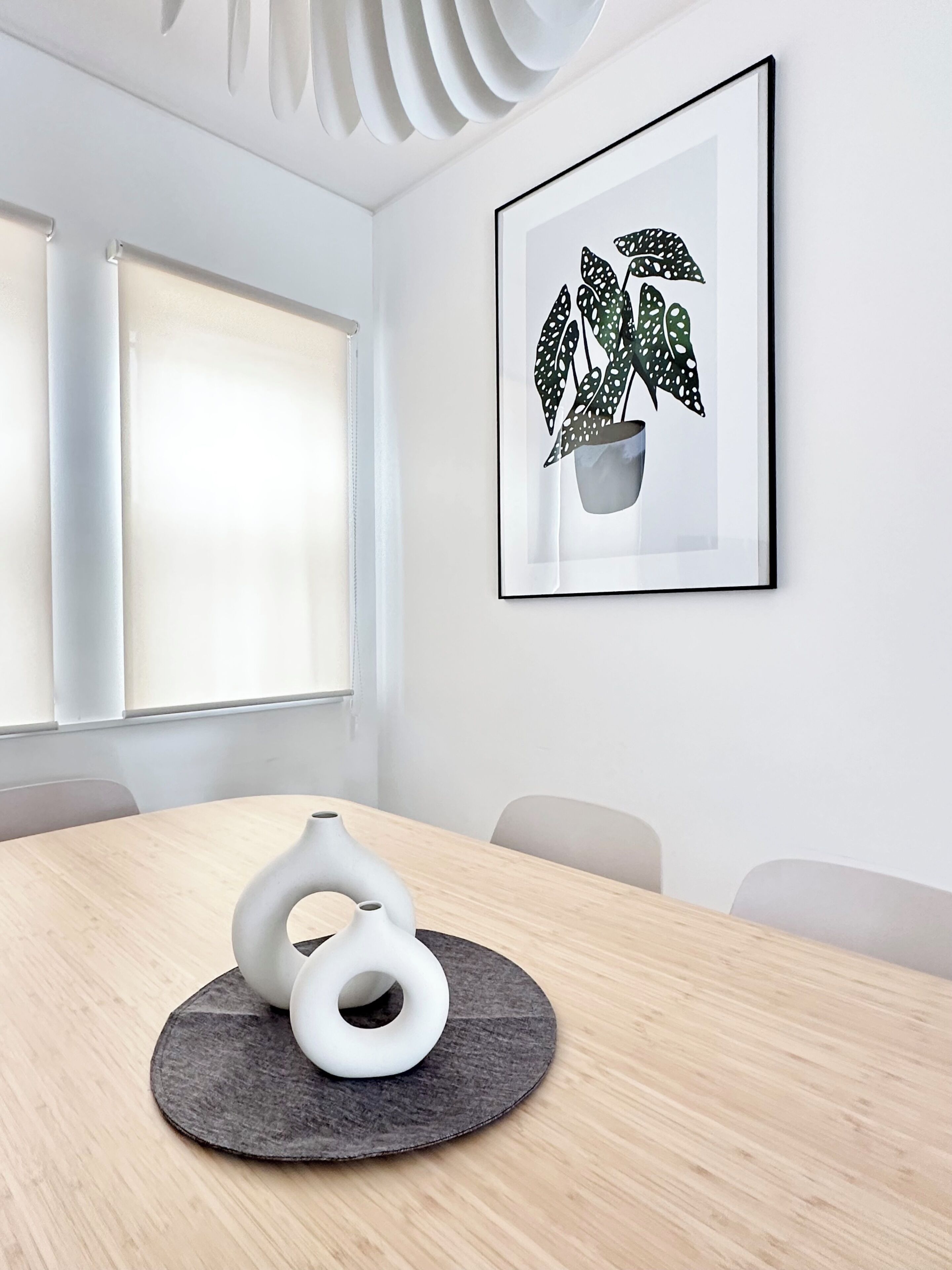 A conference room with a round table, chairs, a framed plant artwork, and a unique white vase.