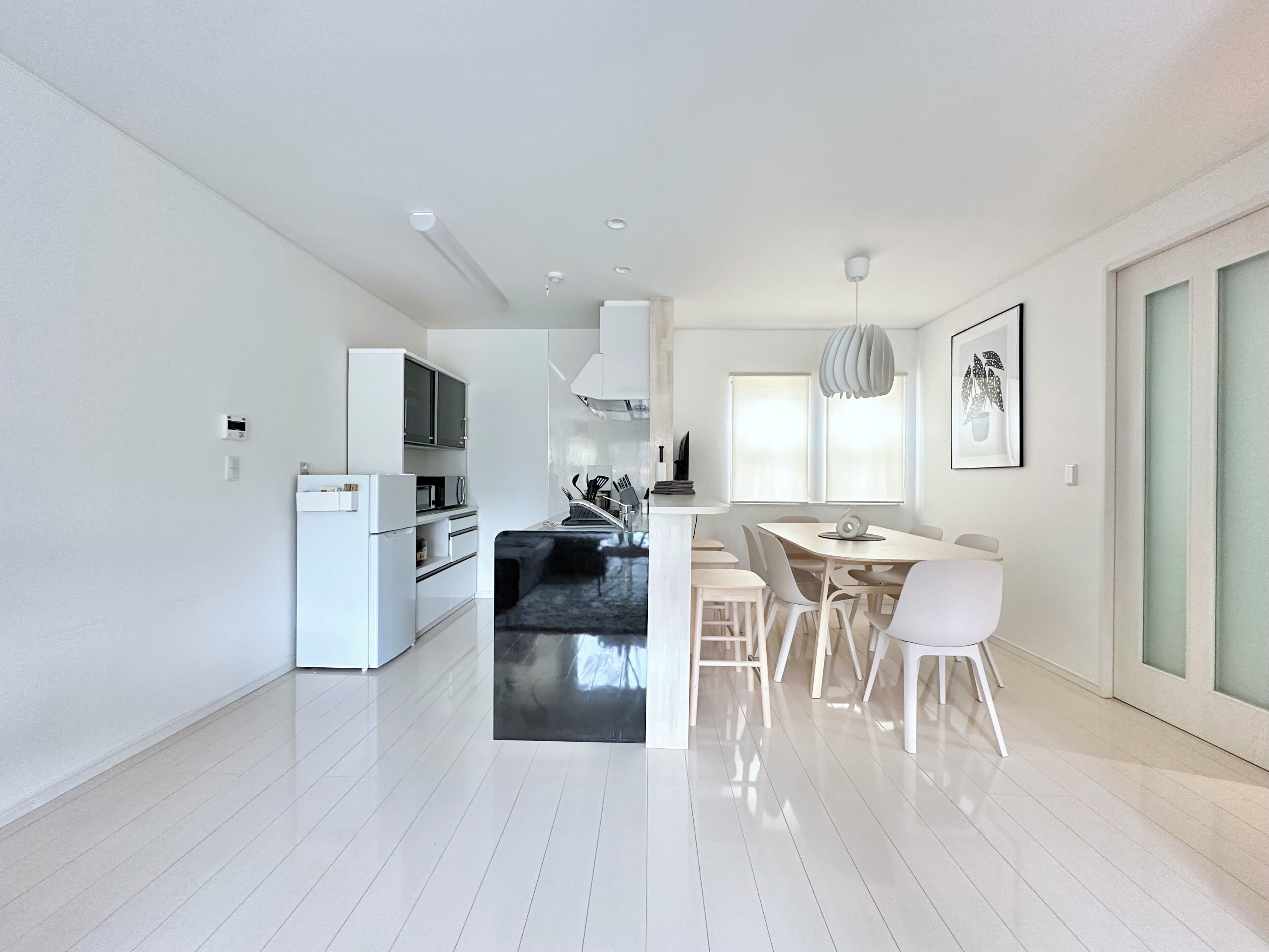 A modern kitchen with white cabinetry, a dining area with a white table and chairs, and a large window providing natural light.
