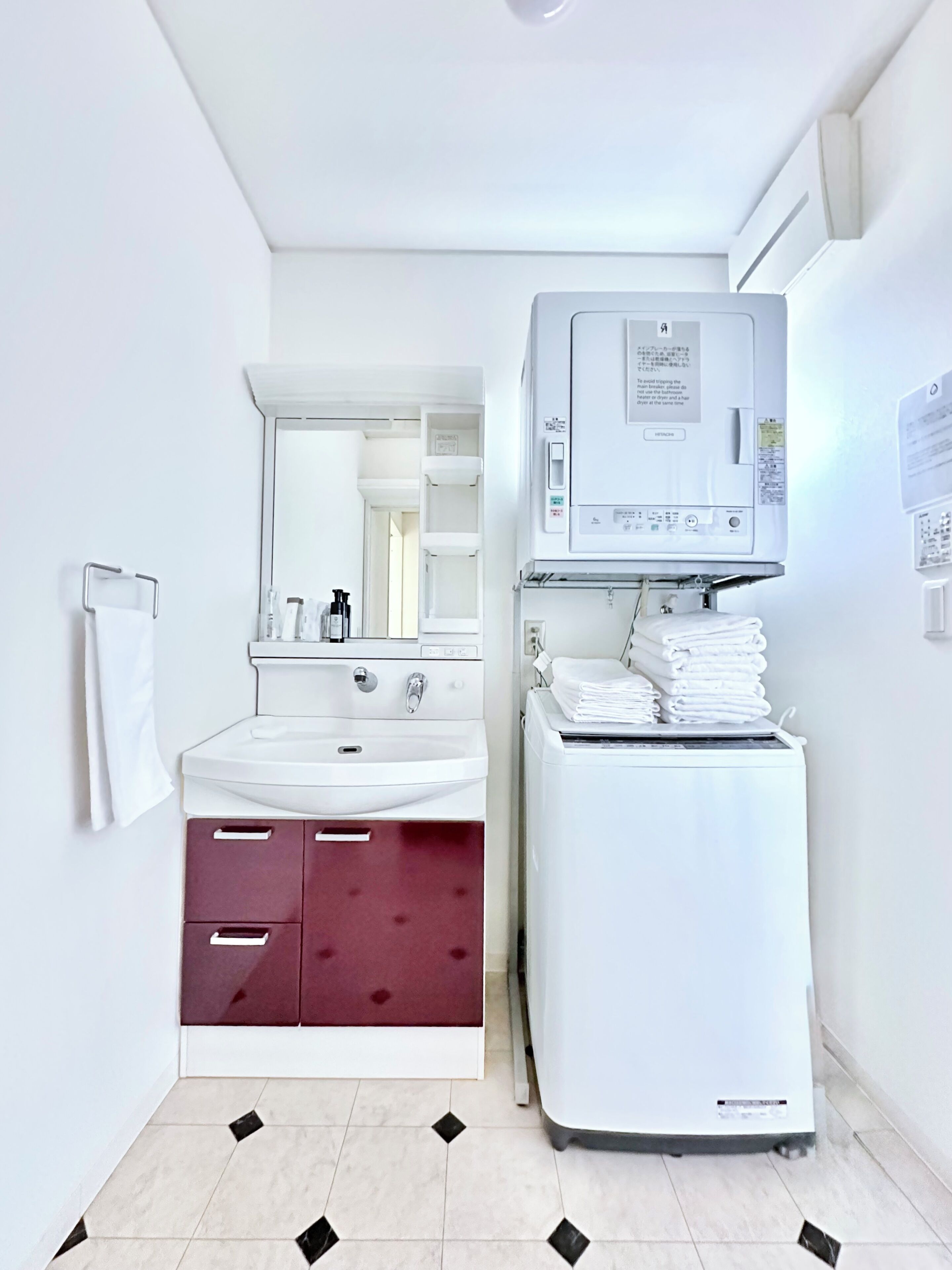 A compact bathroom with a white sink, mirror, and a stacked washer-dryer unit.