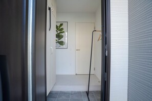 Un couloir avec une porte au fond, une plante en pot accrochée au mur et un porte-manteau.