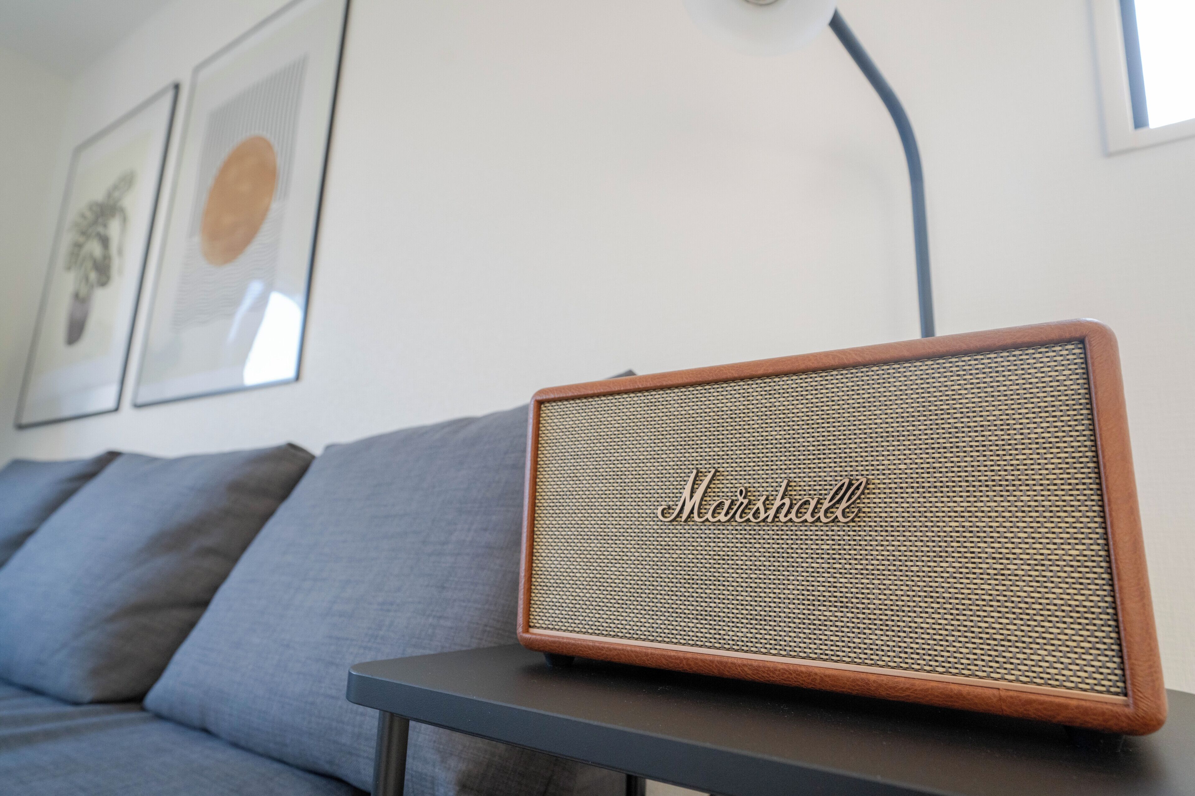 Un altavoz de madera pequeño con la palabra 'Marshall' grabado, sobre una mesa frente a un sofá gris.
