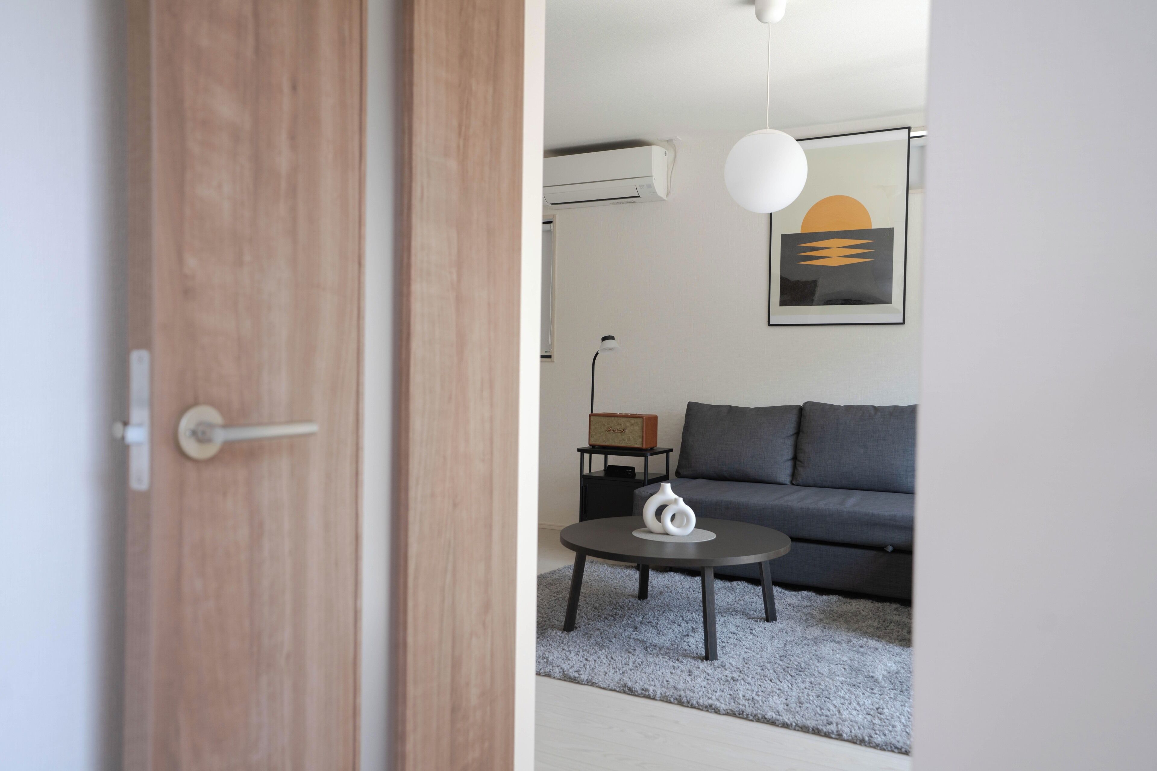 Una sala moderna con un sofá gris, una mesa de centro redonda y un jarrón blanco.
