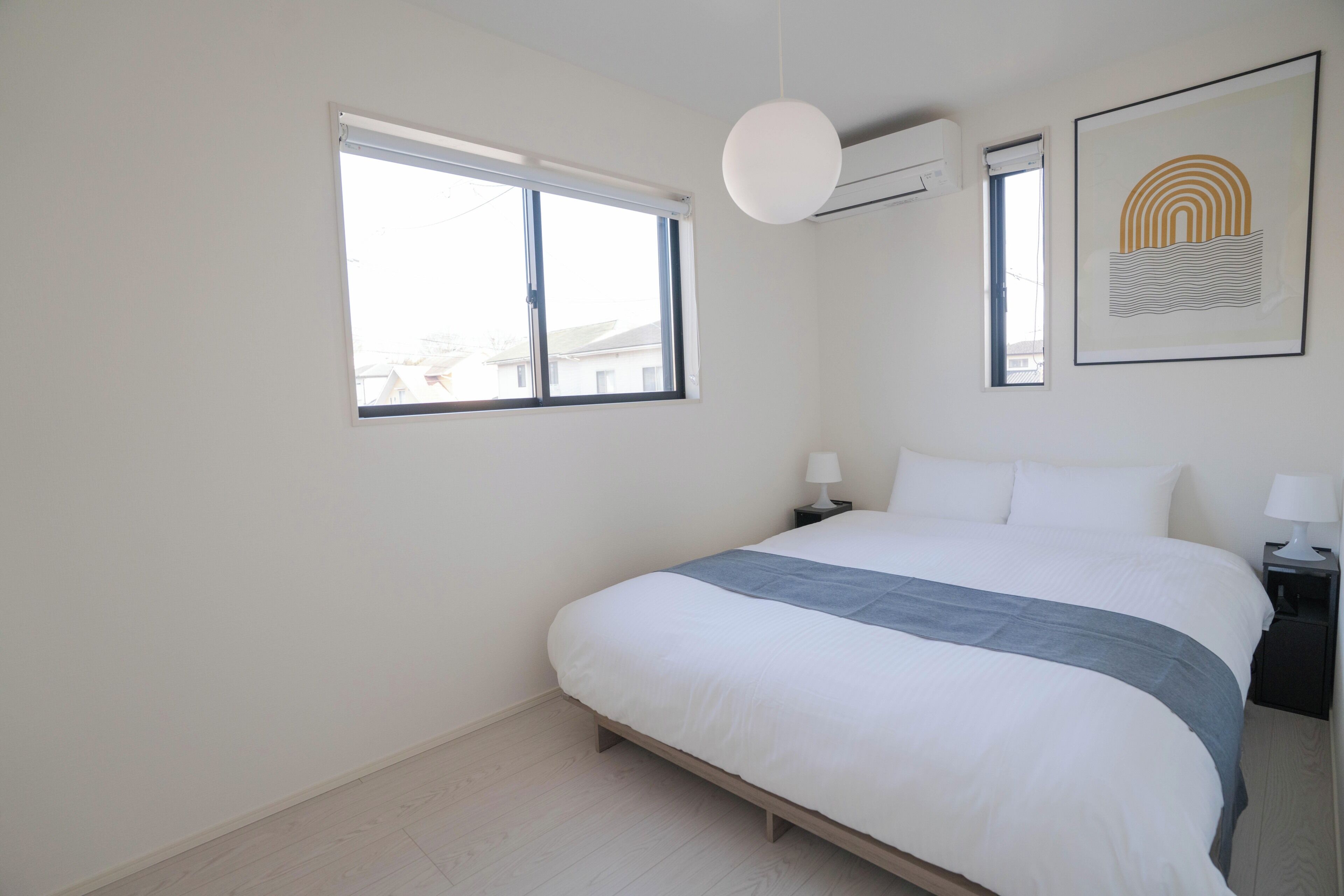 A bedroom with a bed, a bedside table, a lamp, a window, and an air conditioning unit.