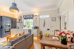 Eine moderne Küche mit grauen Schränken, ein Essbereich mit einem Holztisch und eine gemütliche Sitzecke mit einer Couch.