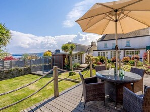 A patio with a round table and chairs, an umbrella, and a view of the sea. - 4 Bed in New Quay (oc-78589) (New Quay)