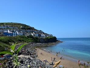 A coastal town with houses on a hillside, a rocky beach, and clear blue water. - 4 Bed in New Quay (oc-78589) (New Quay)