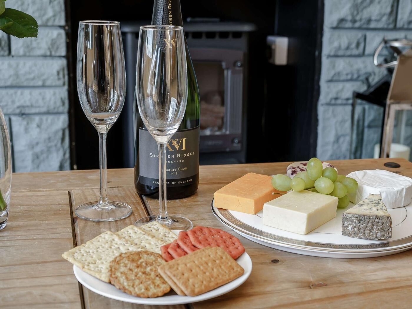 A table with two wine glasses, a bottle of wine, a plate of cheese, grapes, crackers, and a cheese board.