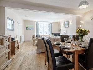 A dining area with a wooden table set for four, a sofa, and a view of the cityscape through large windows. - 4 Bed in New Quay (oc-78589) (New Quay)