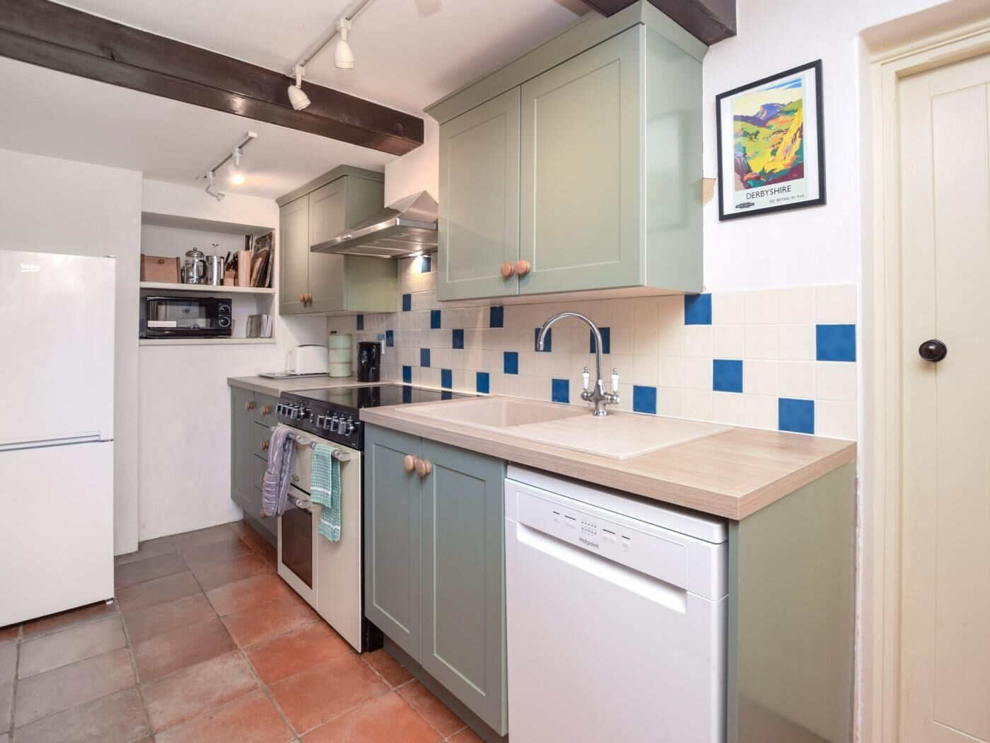 A compact kitchen with a dishwasher, stove, microwave, and a sink with blue-tiled backsplash.