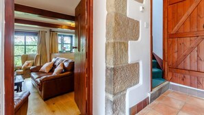 A cozy living room with a brown leather sofa, a stone pillar, and a wooden door. - 3 Bed in Bakewell (oc-78618) (Gratton)