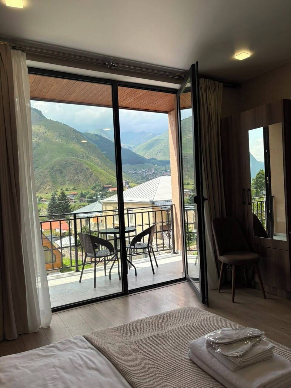 Habitación de hotel con un gran ventanal corredero que da a un balcón y vistas a la montaña.