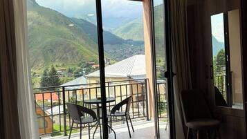 Habitación de hotel con un gran ventanal corredero que da a un balcón y vistas a la montaña.