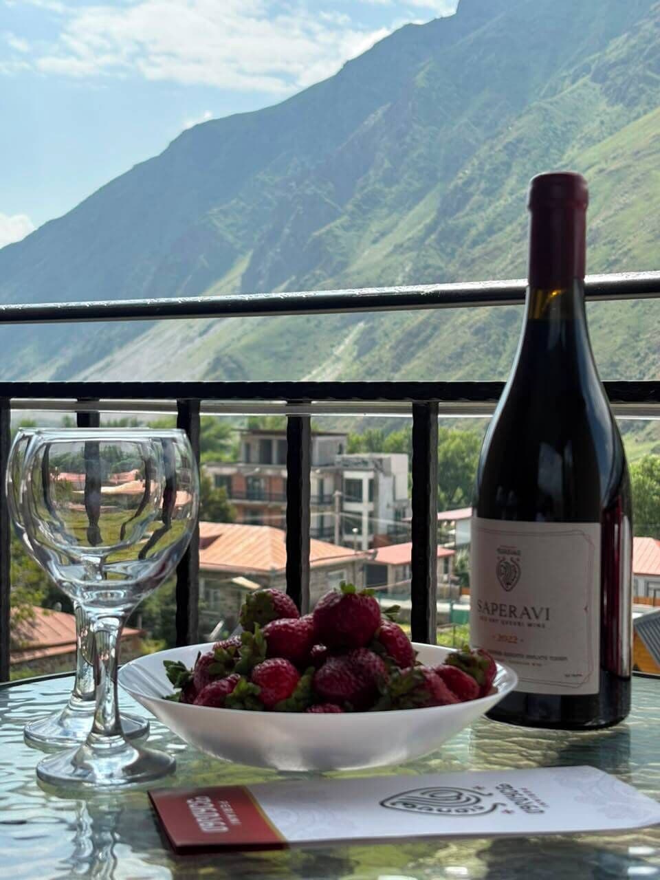 Una mesa con una botella de vino, una copa y un bol de fresas.