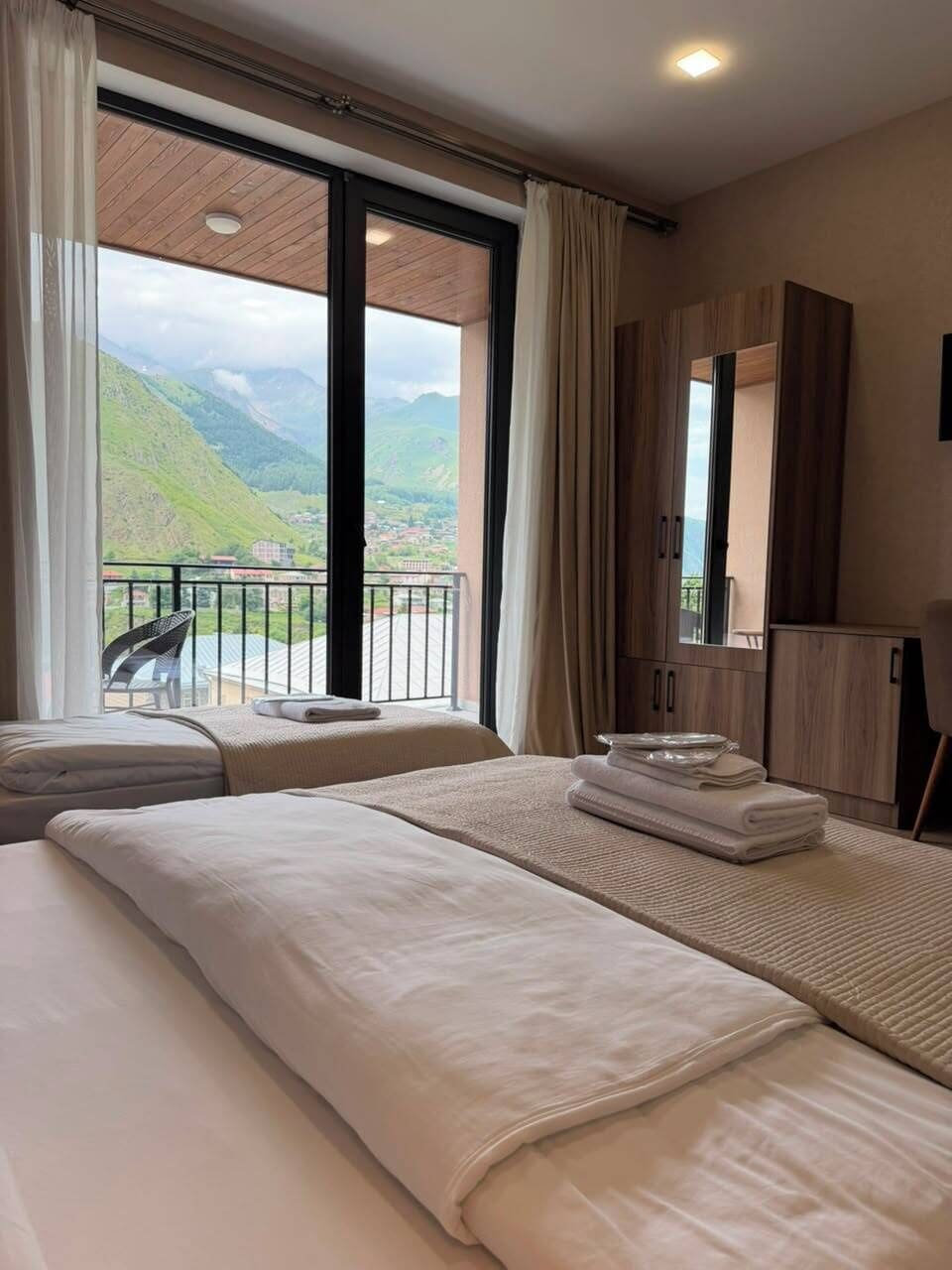 Habitación de hotel con dos camas, un balcón con una silla y vistas a colinas verdes.