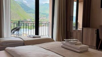 Habitación de hotel con dos camas, un balcón con una silla y vistas a colinas verdes.