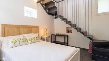 Ein Schlafzimmer mit einem Bett, einem Nachttisch, einem Schreibtisch, einer Treppe und einem Fenster.