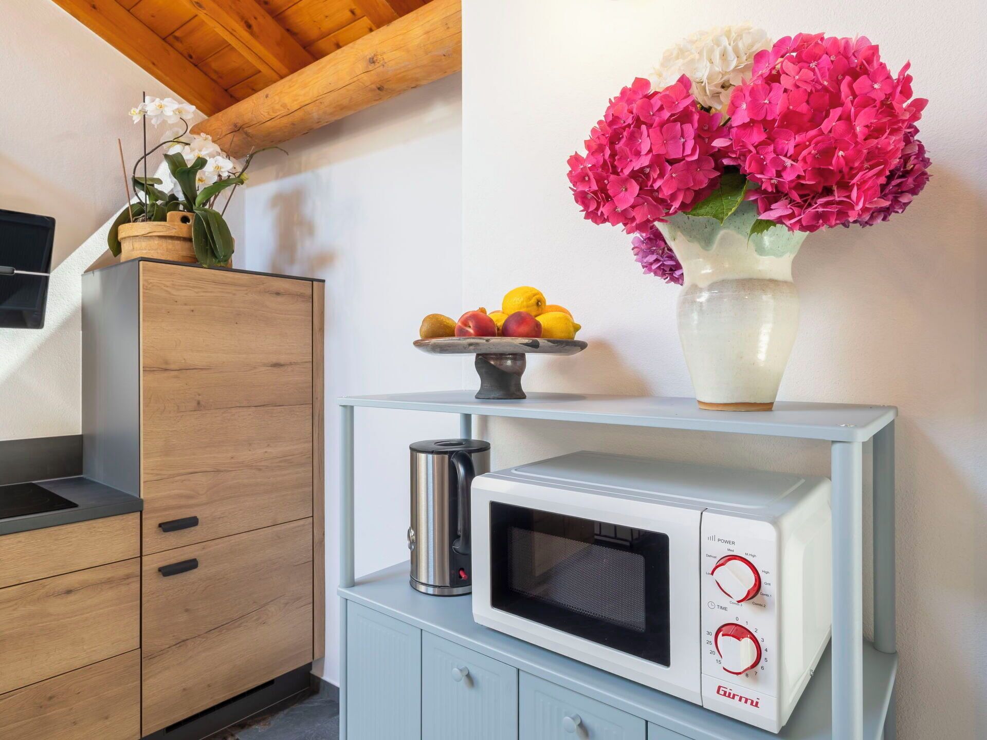 Une cuisine de taille réduite, équipée d’un four à micro-ondes, d’un panier à fruits et d’un vase avec des fleurs.
