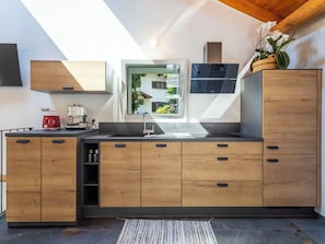 A modern kitchen with wooden cabinets, a built-in oven, and a window overlooking a garden.