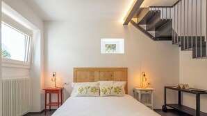 A bedroom with a wooden headboard, a bed with white bedding, two bedside tables with lamps, a radiator, a window, and a staircase. - Stunning private villa for 4 guests with WIFI, TV, terrace and pets allowed (Piuro)
