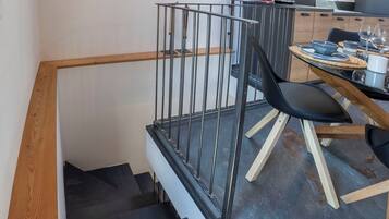 Eine Treppe mit Holzgeländer und Metallhandlauf, die zu einem Essbereich mit Tisch, Stühlen und Küchengeräten führt.