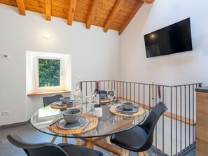 Zona de menjador amb taula de vidre, cadires negres i televisió penjada a la paret.
