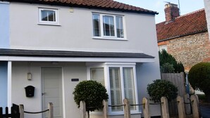 A two-story house with a white exterior, a front door, and two windows with shutters. - 3 Bed in Holt (oc-ncc46) (Holt)