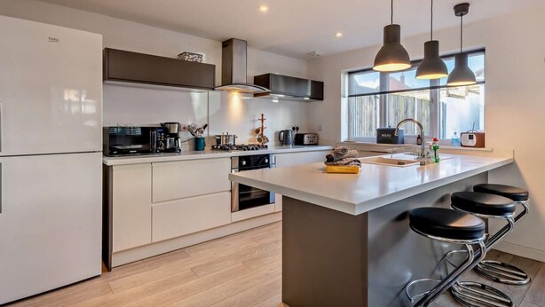 A modern kitchen with a central island, bar stools, a built-in oven, and a large window. - 3 Bed in Holt (oc-ncc46) (Holt)