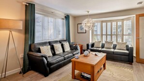 A living room with two sofas, a coffee table, a floor lamp, and large windows with blinds. - 3 Bed in Holt (oc-ncc46) (Holt)