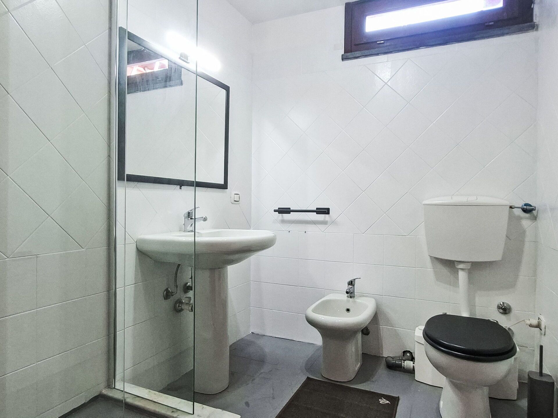 A bathroom with a glass shower enclosure, a pedestal sink, a bidet, and a toilet.