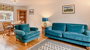 A living room with a teal sofa, wooden chairs, a small table, a bookshelf, and a patterned rug. - 2 Bed in Holt (oc-72898) (Holt)