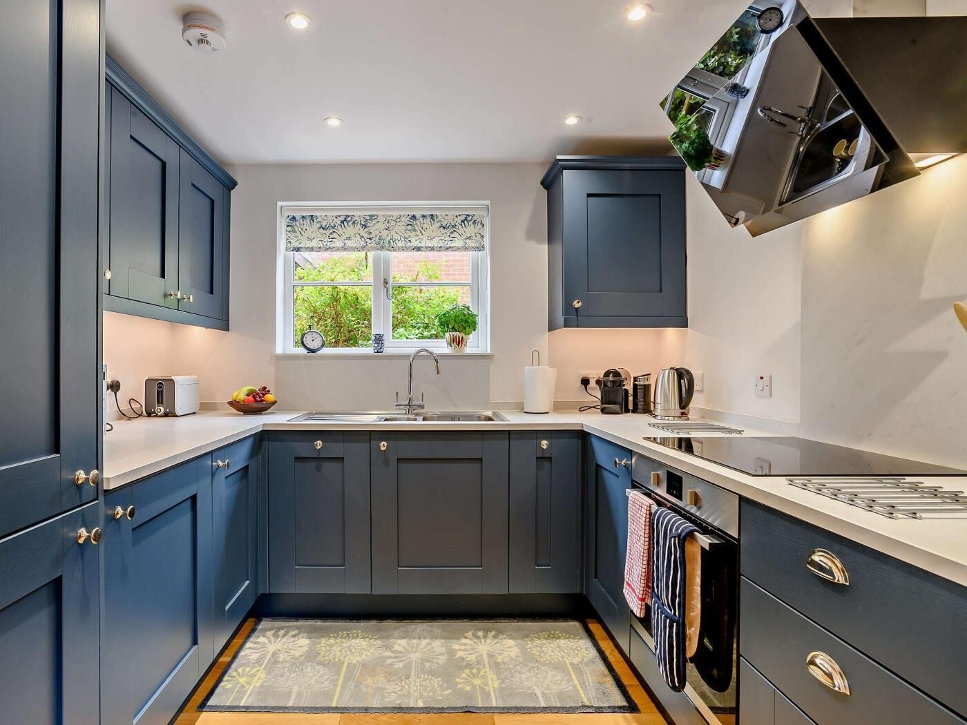 A modern kitchen with dark blue cabinets, a white countertop, a window with a view of greenery, and a built-in oven.