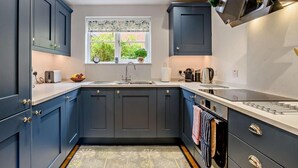 A modern kitchen with dark blue cabinets, a white countertop, a window with a view of greenery, and a built-in oven. - 2 Bed in Holt (oc-72898) (Holt)