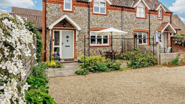A two-story house with a stone facade, a front door, and a small garden with a gravel driveway. - 2 Bed in Holt (oc-72898) (Holt)