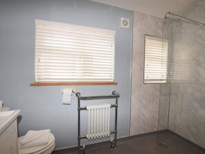 Kylpyhuone, jossa on wc, pyyheteline, patteri ja lasinen suihkuseinä.