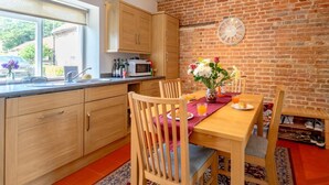 A kitchen with wooden cabinets, a microwave, and a dining table with chairs. - 2 Bed in Holt (oc-ncc66) (Blakeney)