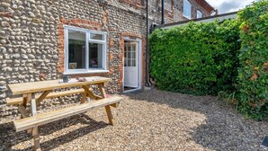A stone building with a wooden bench, a door, and a hedge. - 2 Bed in Holt (oc-ncc66) (Blakeney)