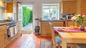 A compact kitchen with wooden cabinets, a built-in oven, a sink, and a dining area with a table set for two. - 2 Bed in Holt (oc-ncc66) (Blakeney)