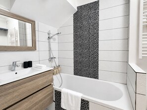 Une salle de bain moderne avec une baignoire sur pieds, un meuble-lavabo en bois, un miroir et une douche avec un mur à texture.