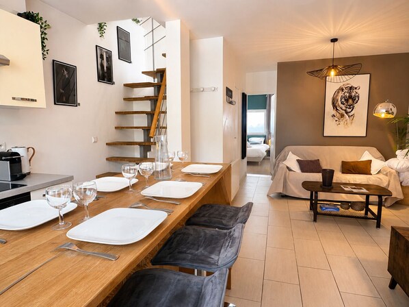 Une cuisine moderne avec une table à manger en bois pour quatre personnes, un escalier et un coin salon comprenant un canapé et une table basse.