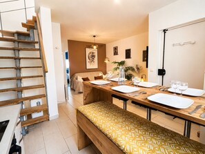 Un espace repas moderne avec un banc en bois, une longue table dressée et un escalier situé à gauche.