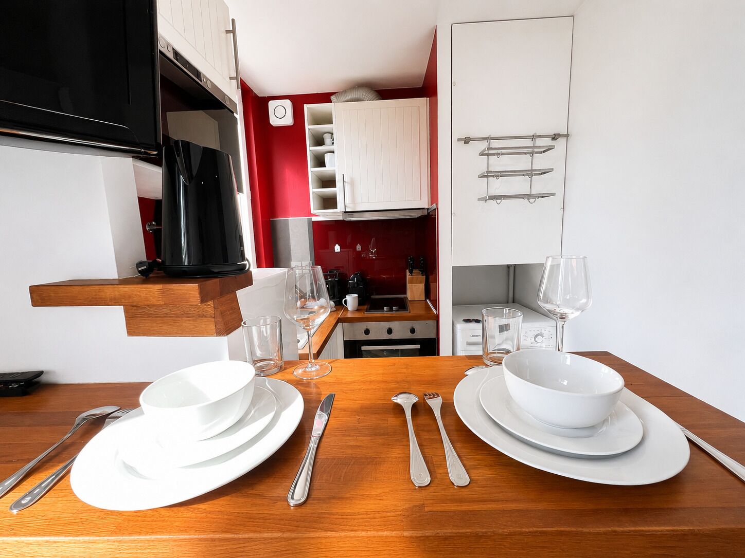 A dining table set with white plates, bowls, and cutlery, a coffee maker, and wine glasses.