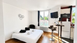Una camera d'albergo con un letto, una scrivania con una sedia, una televisione, un angolo cottura con un frigorifero e una finestra con vista.