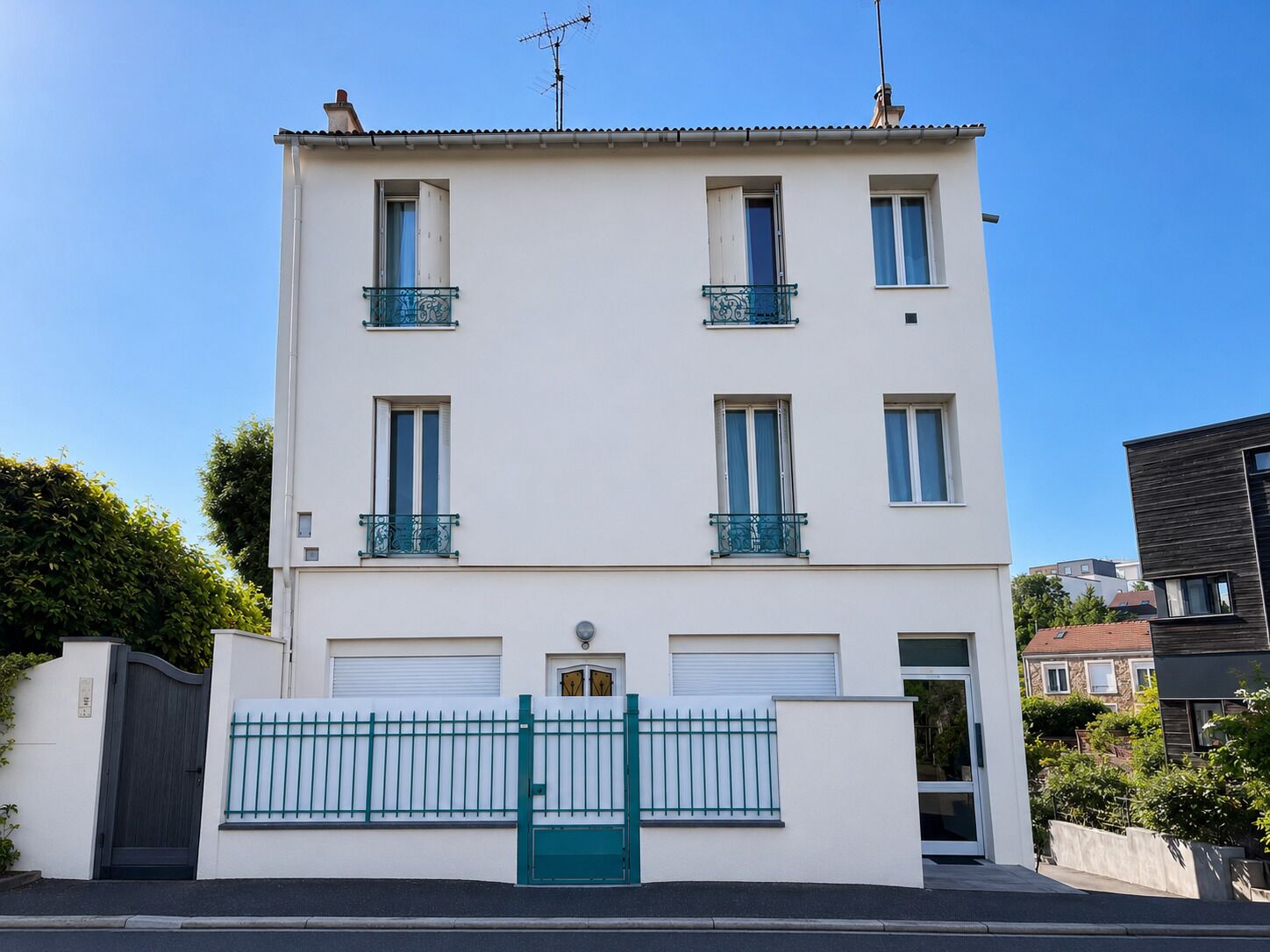 A two-story building with a white facade, balconies with metal railings, and a gated entrance.