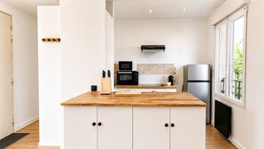 A modern kitchen with white cabinets, a wooden countertop, and a built-in microwave. - Le Verdun | Paris & Disneyland (Fontenay-sous-Bois)